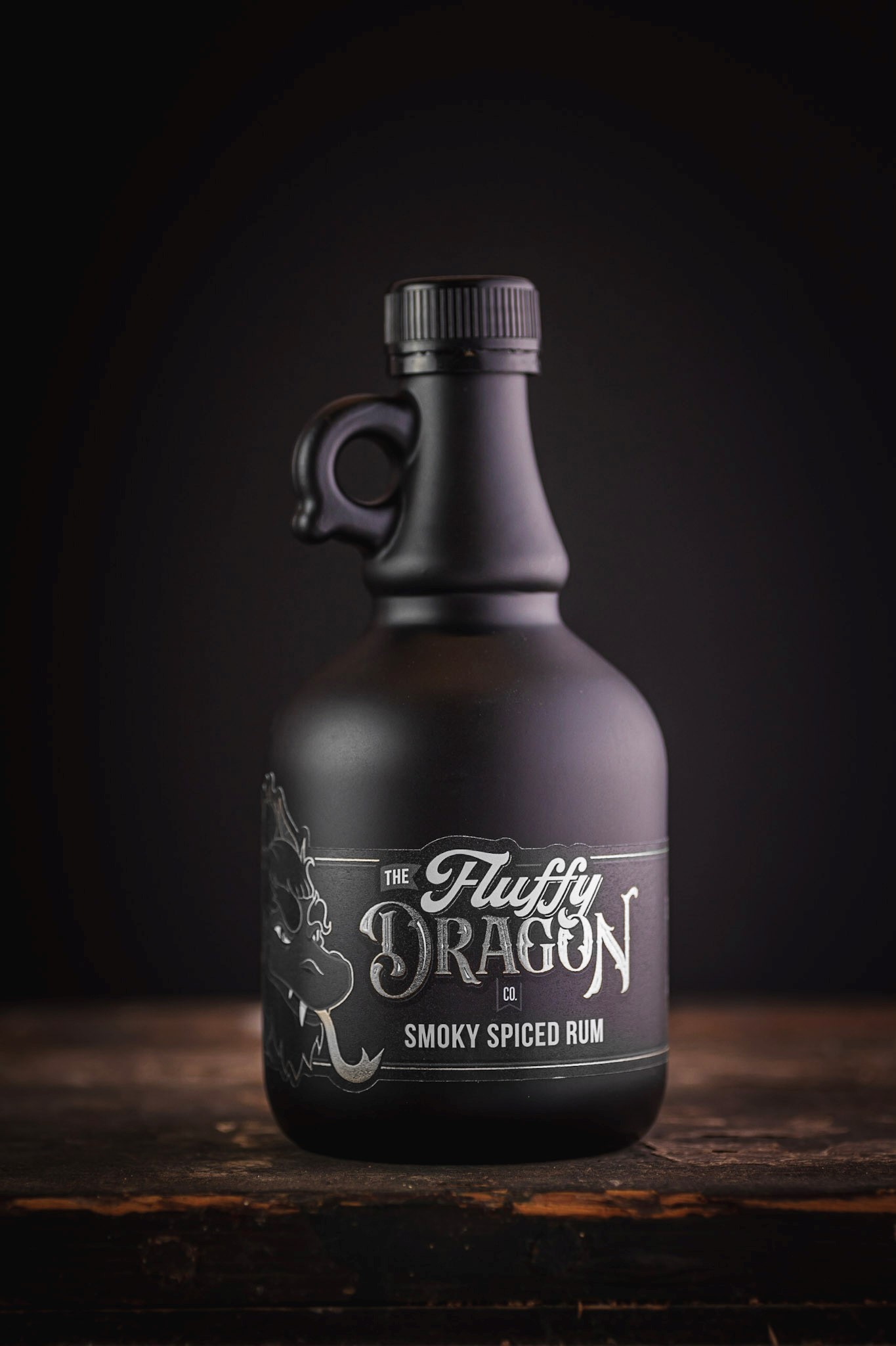 A photo of The Fluffy Dragon Co black bottle on a wooden table with the smoky spiced rum label