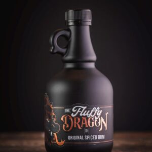 A photo of The Fluffy Dragon Co black bottle on a wooden table with the original spiced rum label